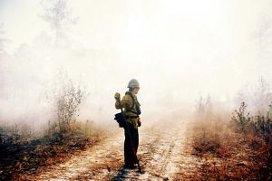 A woman dressed in fire gear is surrounded by smoke. 