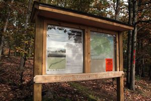 A wooden trail kiosk with a narrow overhangs shades two large information areas showing trial maps and information about the preserve.