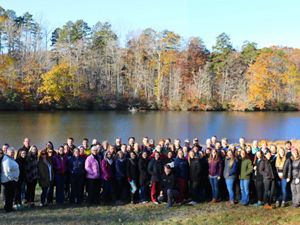 Group photo of TNC VA staff. A large group of people stand together outdoors in front of a calm lake, smiling during the chapter's annual staff retreat.