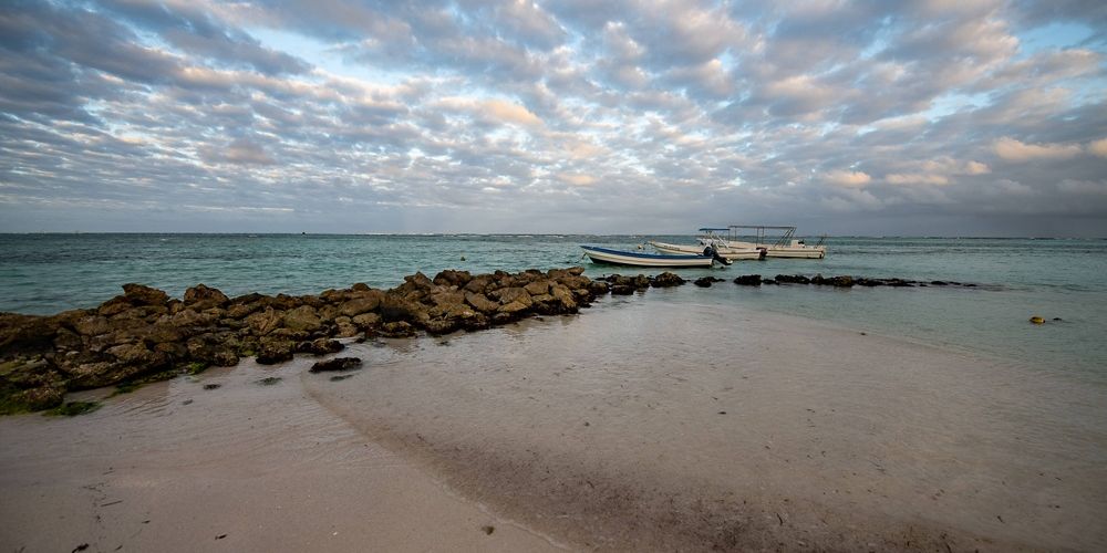 rock jetty stretching out in blue ocean water with soft clouds above