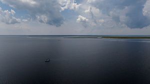 Aerial drone view looking down on a small skiff. The boat is a small speck in the wide expanse of a coastal Atlantic bay.