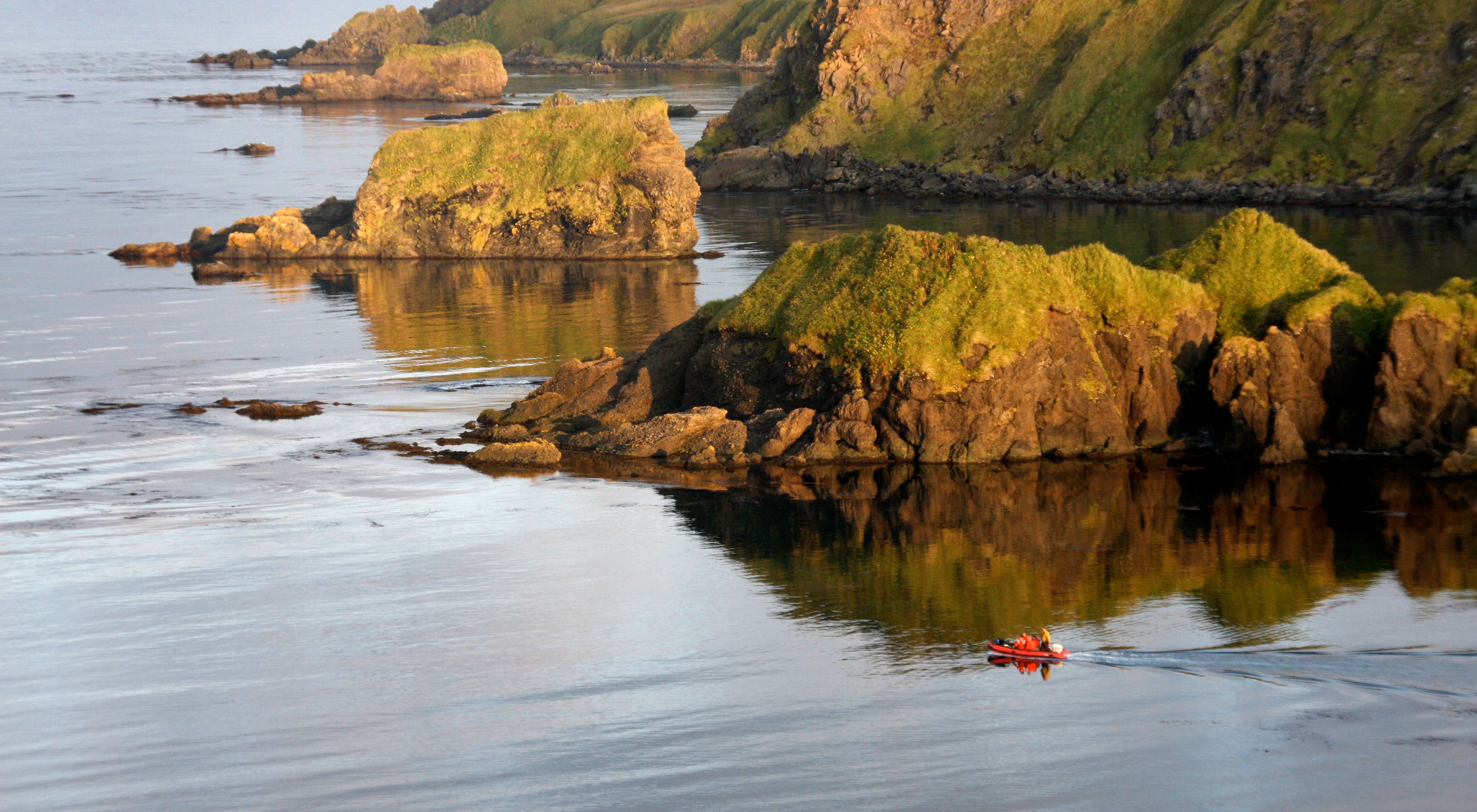A small red dinghy is dwarfed by the rocky shoreline of Hawadax Island.