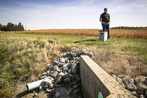 Man stands next to water structure on ag field.