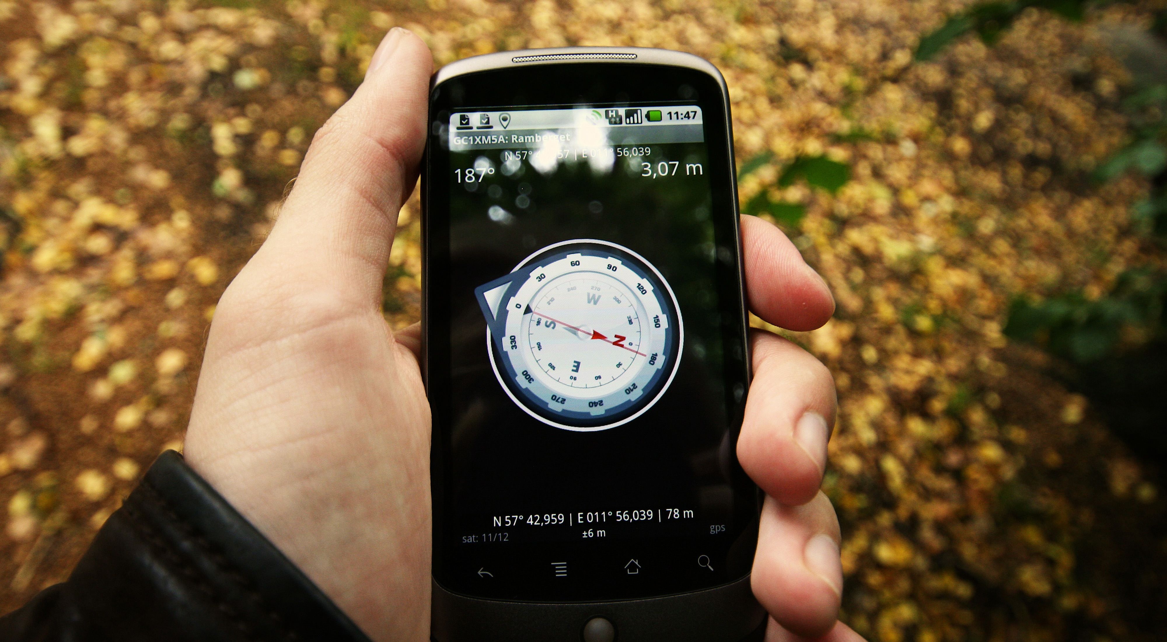 A man holds a cell phone showing map coordinates.