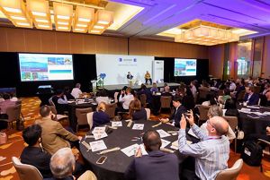 People gather in a conference room two watch two speakers sitting on a stage. 