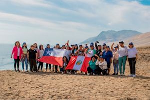 Grupo de mujeres de la pesca en una playa sosteniendo banderas de Chile y Perú. 