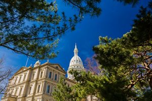 The dome of Michigan's statehouse framed by tree branches and a bright blue sky in downtown Lansing. 
