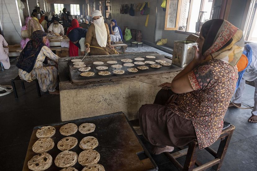 A woman tends to dozens of flat breads on a large stove as other community members work in the background.