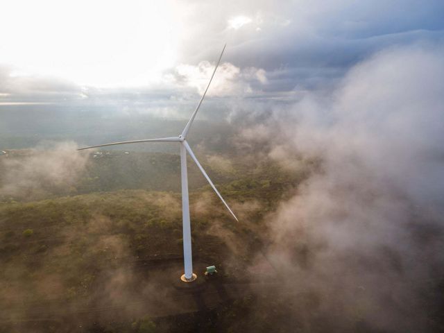 Morning mist rolls up from the valley floor below wind turbines from Kipeto Wind Farm at sunrise. 