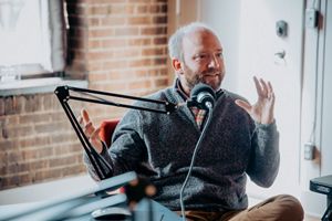 Adam McLane sitting at table talking into microphone.