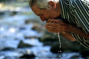 Proprietário rural lava o rosto com água em beira de rio