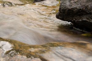 Água correndo próximo a pedras na beira de um rio.