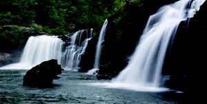  A wall of rock with a dramatic series of waterfalls flowing into a waterbody below.