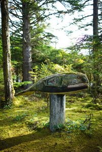 Closeup of a wooden totem of a whale mounted atop a wooden post in a forest.