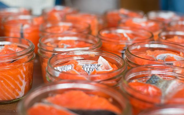 Closeup of several glass jars filled with pieces of fresh salmon.