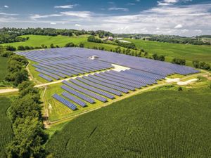 Solar energy farm amid green farmfields and blue sky.