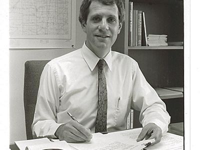 Alan Pollom sitting at desk holding papers