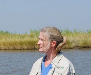 A woman with a blue shirt and a ponytail looks out over some water.