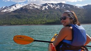 A photo of the author sitting in a kayak on a body of blue water with mountains in the background.