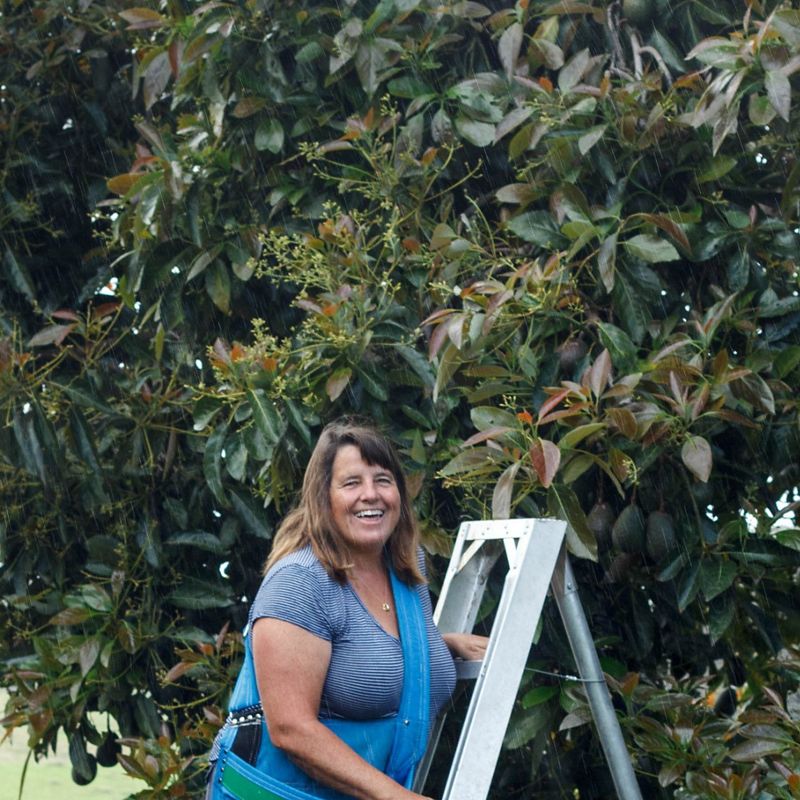 Woman smiles at camera in front of an avocado tree.