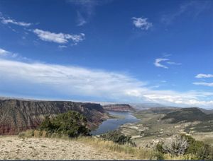 View looking down a wide valley bordered on one side by towering red sandstone cliffs. A wide river flows through the bottom of the valley.