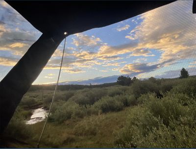 Looking out through the open window of a tent, the clouds overhead are painted golden by the rising sun.