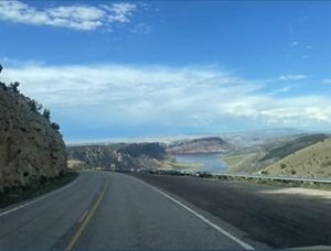 A two-lane highway curves around a bend toward distant mesas. A large lage is visible in the valley below.