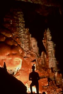 The silhouette of a person stands in a lit-up,  orange cave. 