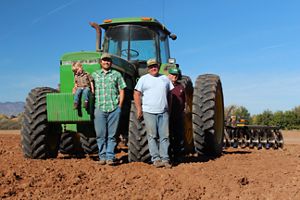Three adults and a child stand in front of a green tractor on a sunny day. 