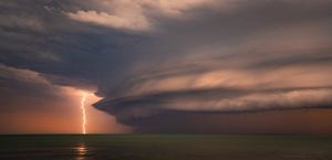 A lightning strike in the distance against a peach coloured storm clouds