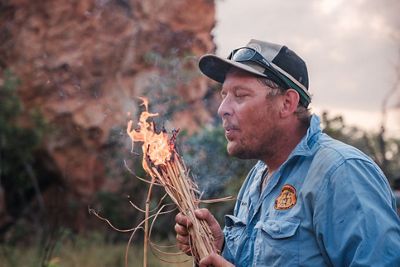 a fire ranger holding a bundle of sticks that are on fire.