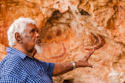 a man standing in front of a red rock wall covered in ancient art.