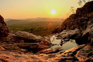Two people sitting on the edge of a rock pool overlooking bushland at sunset