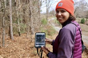 Lauren Goodman stands by a forest tract holding a tablet.