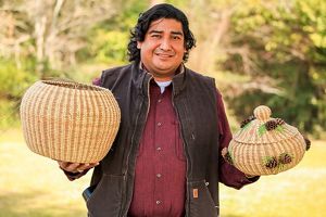 A man stands holding a large basket and a small basket adorned with pinecones.