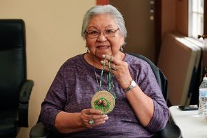 A woman holds up a colorful woven pendant necklace.