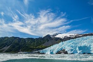 A large, jagged glacier flows down into a body of water framed by mountains.