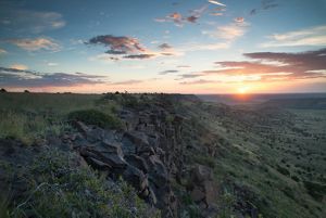 The sun sets behind a jagged rock formation.
