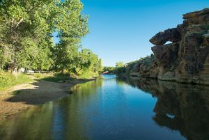 A creek bordered on either side by rock formations and native trees.