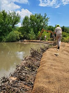 A person in construction gear walks to right side of a body of water where the surrounding land is being actively worked on by heavy machinery and construction personnel. 