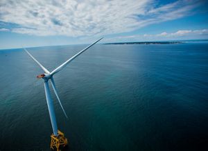 A wind turbine sits in the middle of a blue ocean.