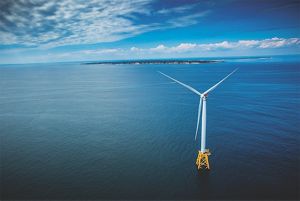 An aerial view of a wind turbine in the ocean, with the coast of Block Island and Rhode Island in the background.