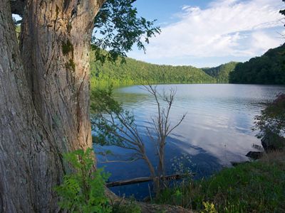 Green forested mountains surround a calm, clear pond.