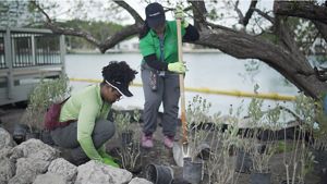 Two women work together to dig holes and plant native vegetation.