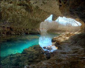 A cave opening with turquoise blue clear water in it. 