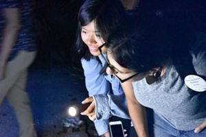 Two women observe insects at night.