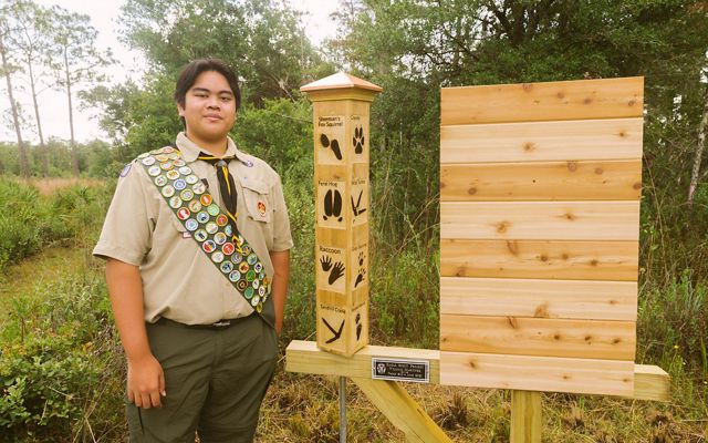 Eagle Scout standing beside a wooden public exhibit at Tiger Creek Preserve. 