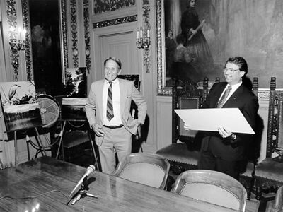 A black and white photo of two people smiling in a board room.