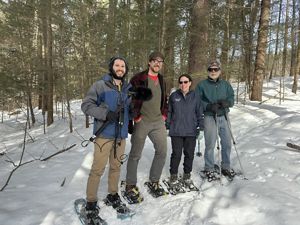 Four people stand in a snowy forest wearing snowshoes. Podcast producer Jay Feinstein is on the left, wearing headphones and holding a boom microphone, next to him are the forester who worked on the land, TNC's Laura Marx, and the owner of the land.