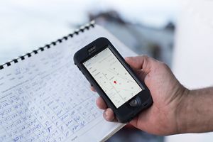 A hand holds a cell phone showing fish catch data.